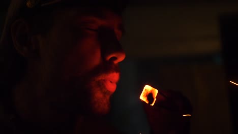 guy blows on a piece of hookah coal in dark background. close up