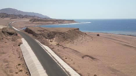 aerial flying over dunes, road and sea at tabuk beach on sunny day, saudi arabia