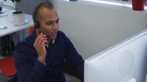hombre de negocios de raza mixta sentado usando computadoras hablando con auriculares de teléfono