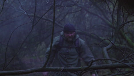 exhausted adult man walking through foggy and rainy forest in wilderness