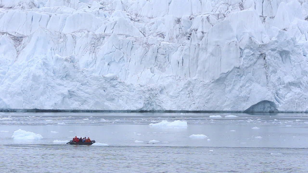 조디악 보트를 타고 있는 관광객들이 알래스카 글래시어 베이의 거대한 빙하에 접근합니다.