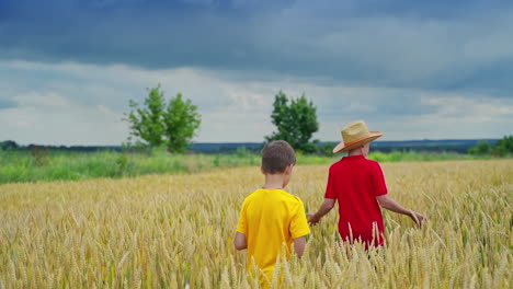 little farmers in yellow field. elder brother in straw hat walking along the wheat field and telling something to his younger brother.