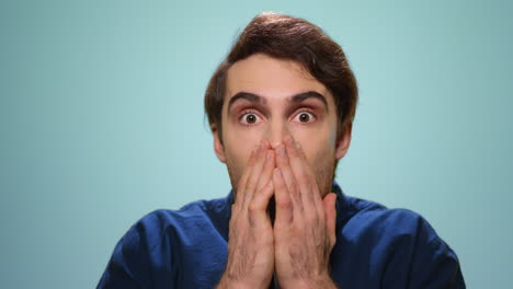 shocked man covering mouth with hands. man with open mouth on blue background