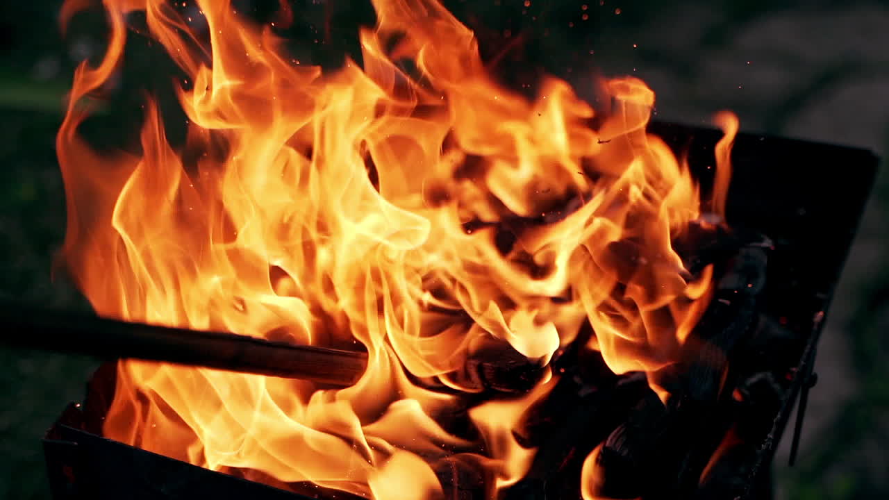 Wooden stick turning over smoldered wood inside bright fire. Exposition of bright flame after moving logs in the fire. Slow motion.