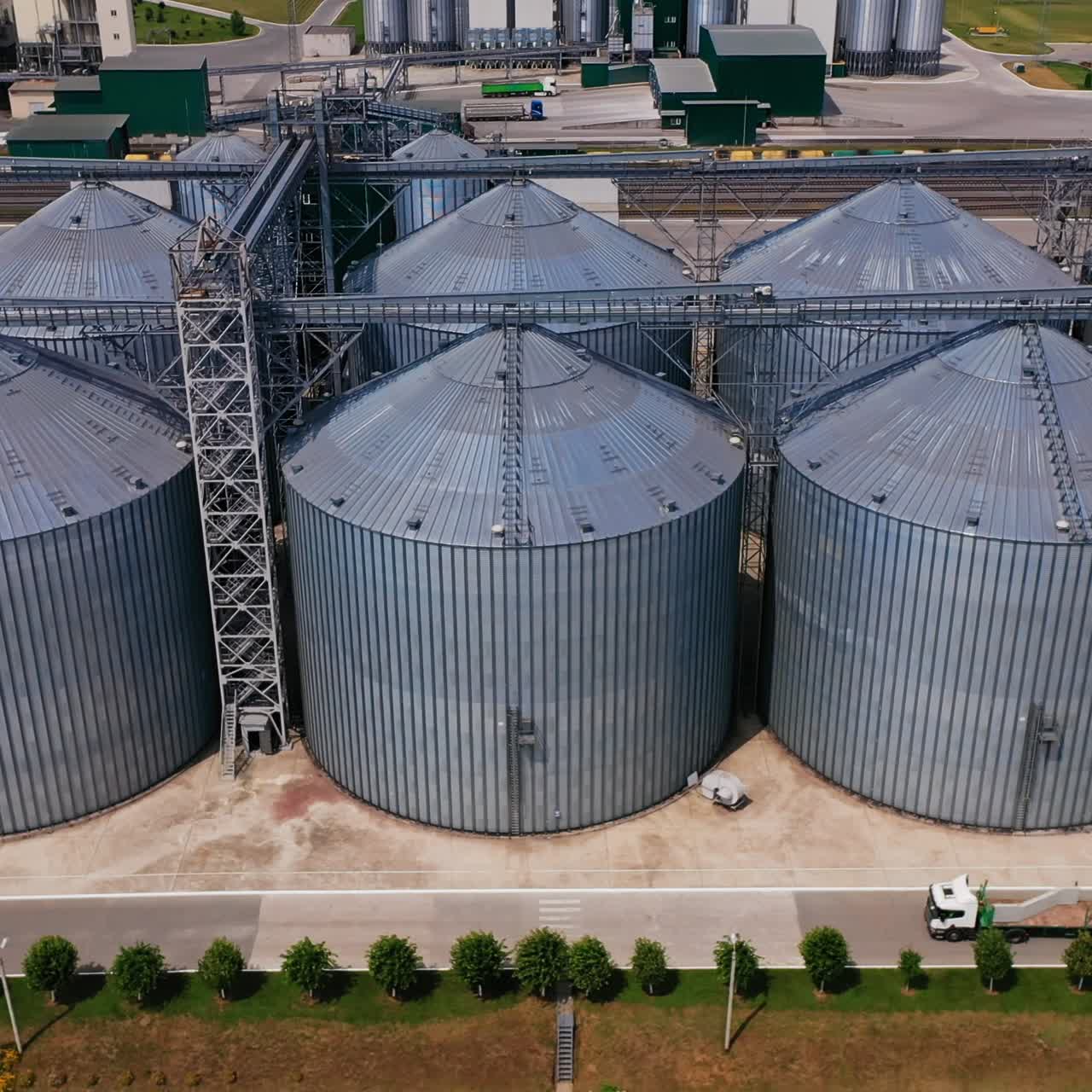 Grain storage bins for agricultural crops. Silver tanks of modern agribusiness plant outside. Aerial circle movement over the well-organized factory area