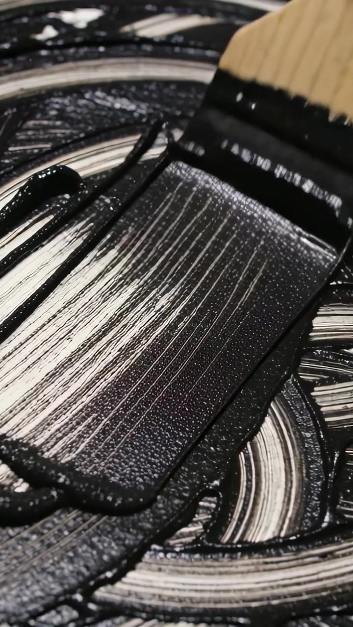 Vidéo verticale : Main appuyant sur un pinceau traînant de la peinture noire en studio, couvrant des marques circulaires.