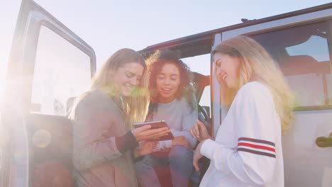 three young women on a road trip using tablet by their car