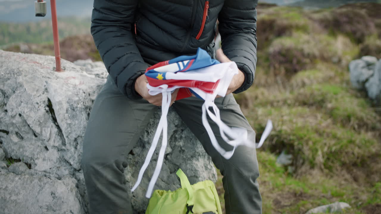 등산객이 바위에 앉아 배낭에서 슬로베니아 국기를 꺼내 눈에 보이도록 바위 위에 펴는 사진을 클로즈업