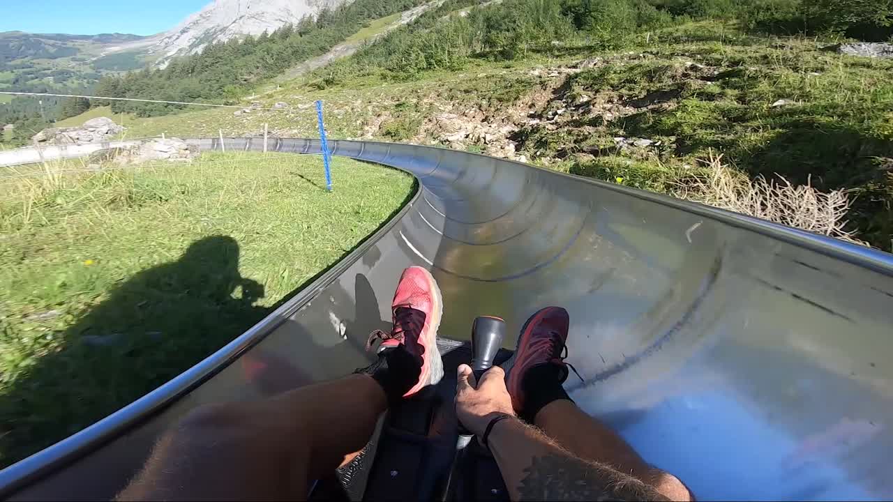 POV shot of a man holding onto a small toboggan, sliding down a long metal slide through the beautiful scenery of the Swiss alps