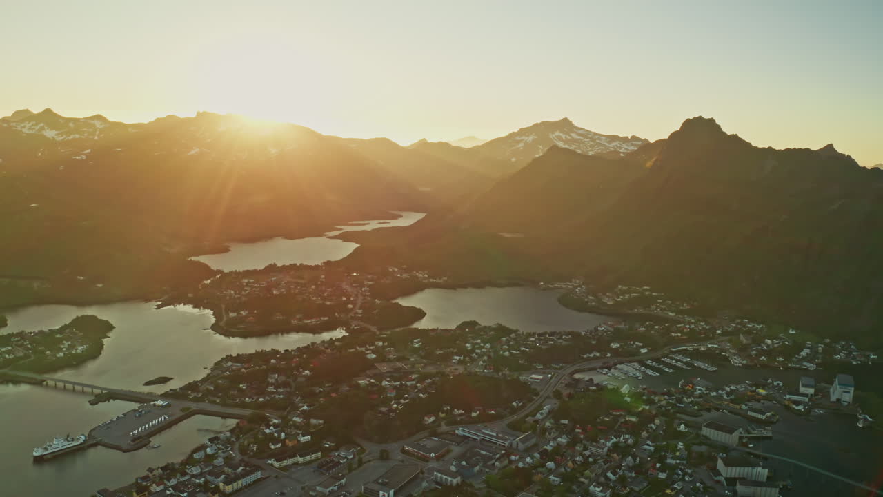 Aerial drone shot over the Norwegian town of Svolvaer in the Lofoten Islands, Norway. Bird's eye view of the fishermen's town at the midnight sun. View of the vast mountains in the background.