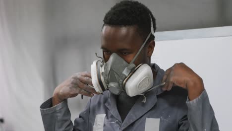 African-American-male-car-mechanic-working-in-a-township-workshop-and-putting-on-a-face-mask