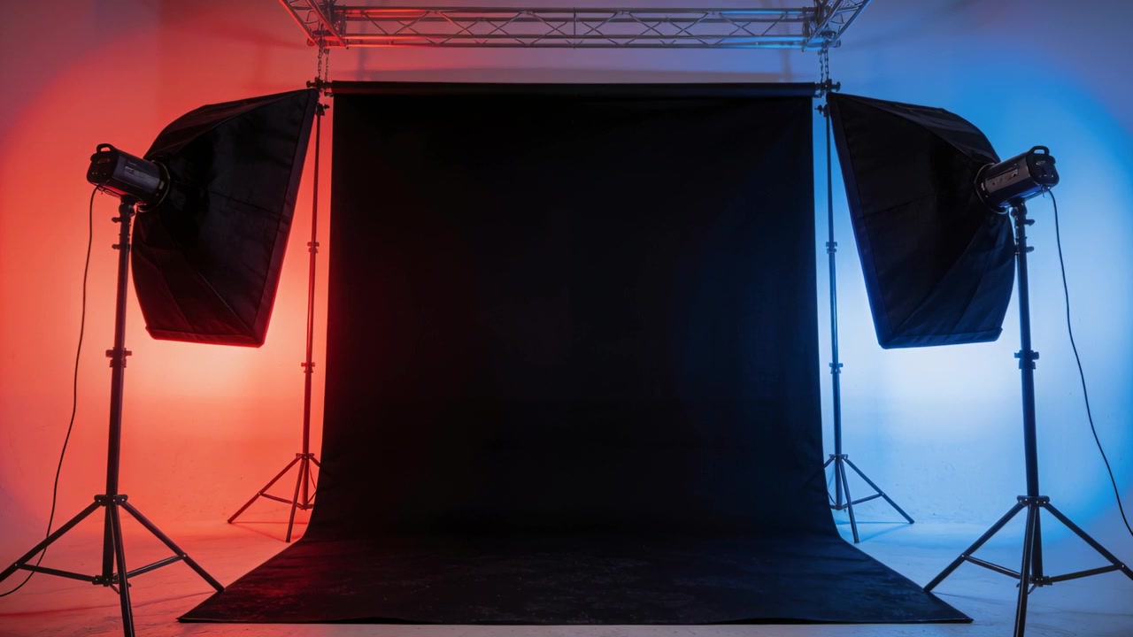 Powering on softboxes, red-blue lights projecting wash in studio, lighting black seamless backdrop