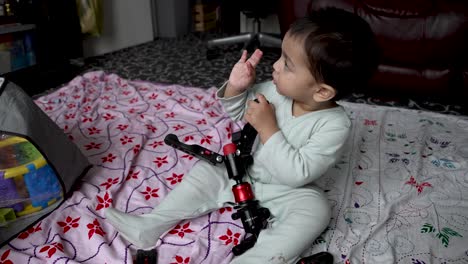 a toddler, 18 months old, joyfully engages with a camera tripod, exemplifying the essence of childhood play whilst waving at television, sitting on the floor