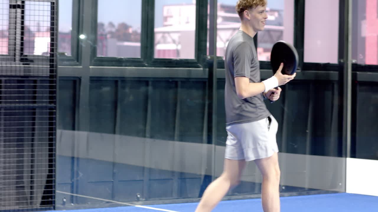 Young man playing padel tennis, preparing to hit ball on indoor court