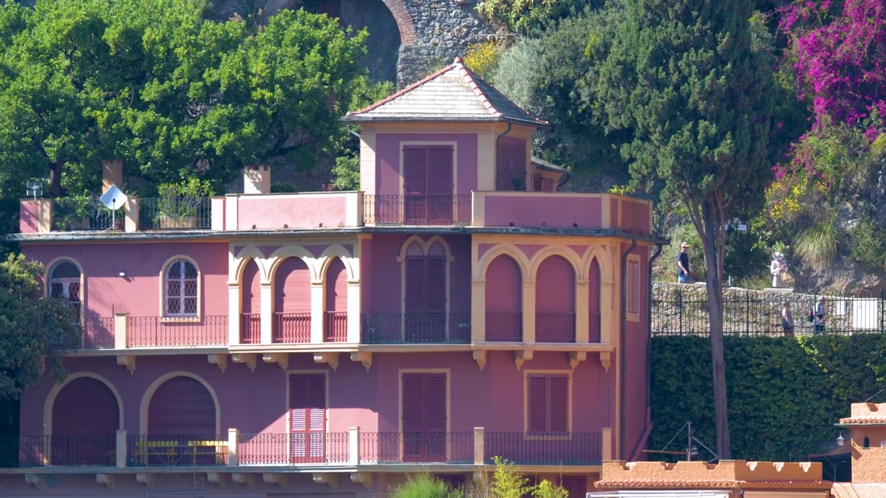 Um zoom lento revela uma vivenda rosa vibrante aninhada entre árvores verdes e buganvílias