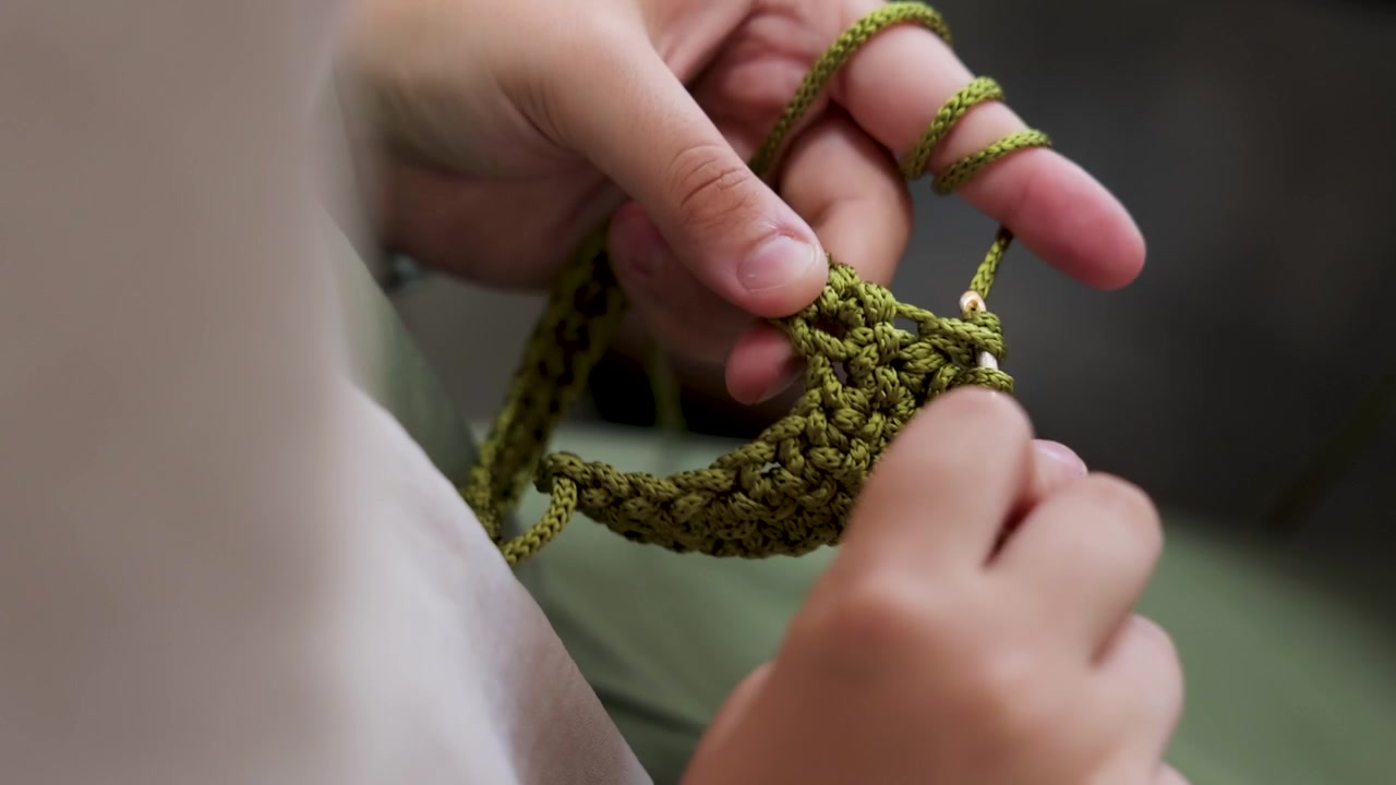 Detailed close-up of hands crocheting green yarn with a crochet hook, showing the technique and texture of handmade textile craftsmanship and traditional handwork.