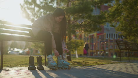 a person sitting on a bench in a park, loosening the straps of one rollerblade while wearing another. the scene captures a quiet moment of transitioning from skating to regular footwear