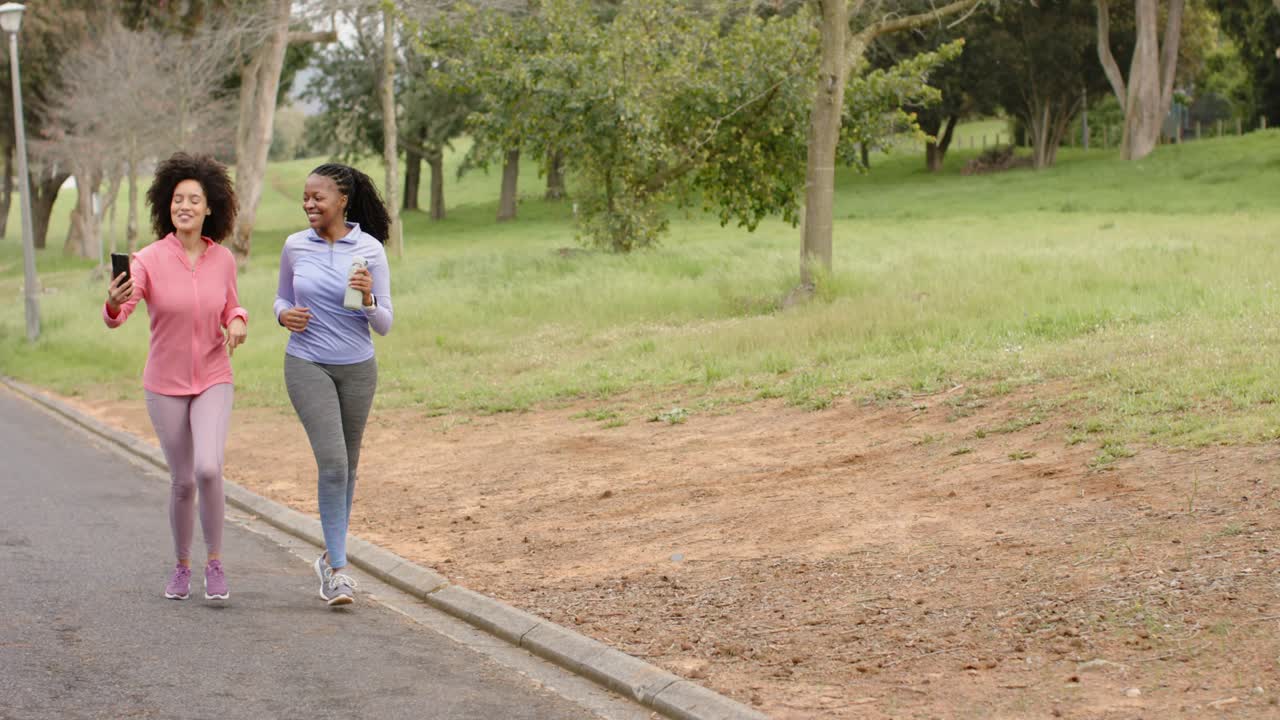 Diverse amiche che fanno jogging su un sentiero, tengono in mano un telefono e una tazza mentre registrano la corsa, spazio libero