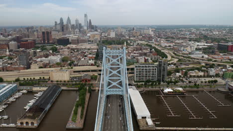 aerial view moving forward of philadelphia ben franklin bridge and skyline in the summer with cars and traffic driving on the road into the city