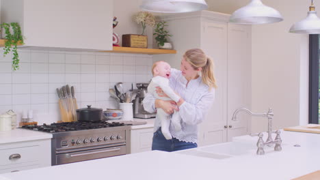 Madre-Amorosa-Llevando-A-Su-Hijo-Riendo-Alrededor-De-La-Cocina-En-Casa-Jugando-Juntos