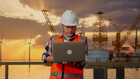 ingeniero masculino asiático con casco de seguridad trabajando en una computadora portátil mientras está de pie con la producción de hidrógeno en alta mar