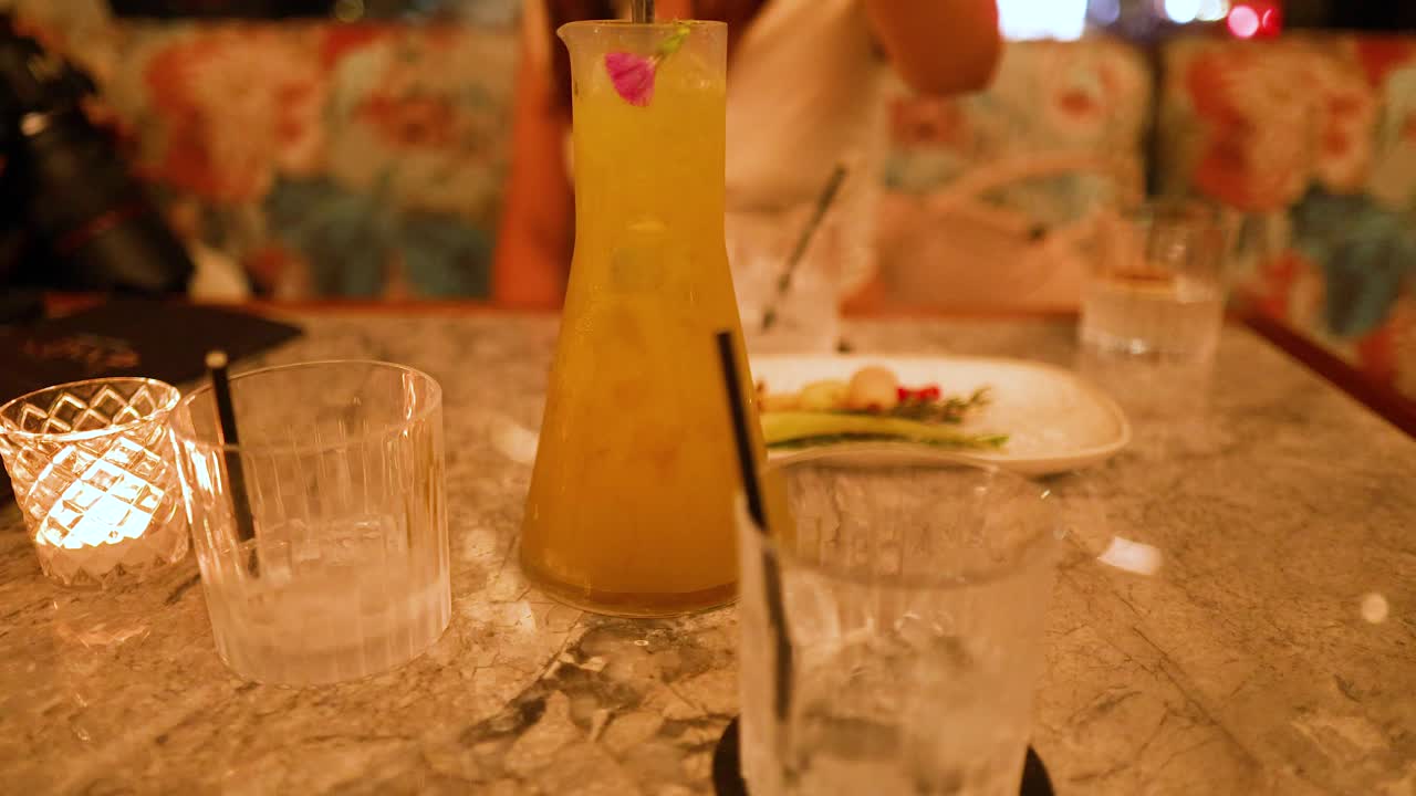 A vibrant cocktail is poured at a dimly lit restaurant table, creating a warm and inviting atmosphere