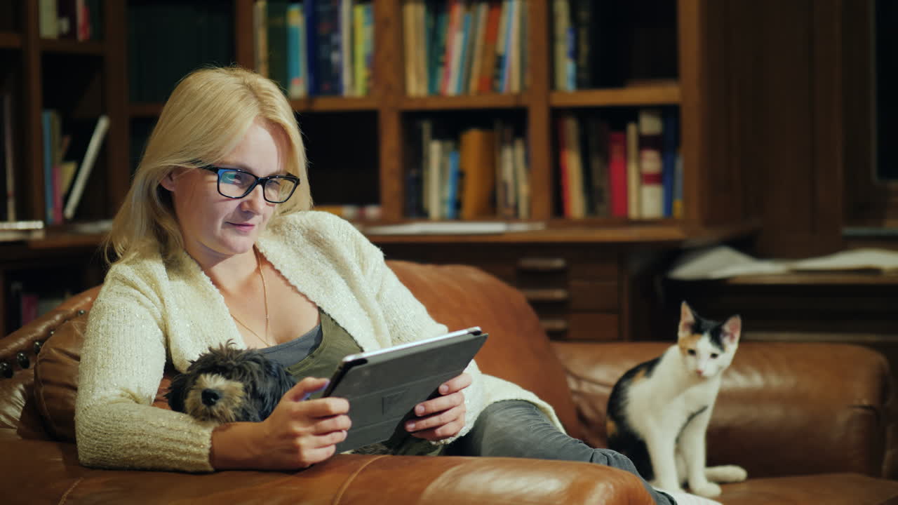 한 여성이 태블릿으로 책을 읽고 고급스러운 도서관 뒤편에 앉아 있습니다.