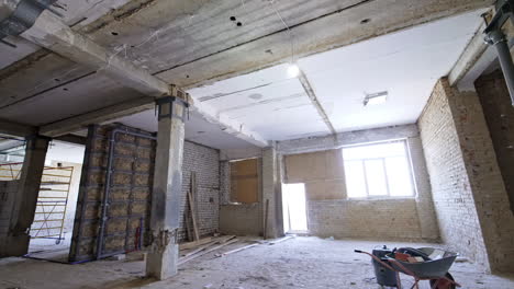 large room with columns and shabby walls. some walls are newly built. windows are covered with chipboard. building renovation.
