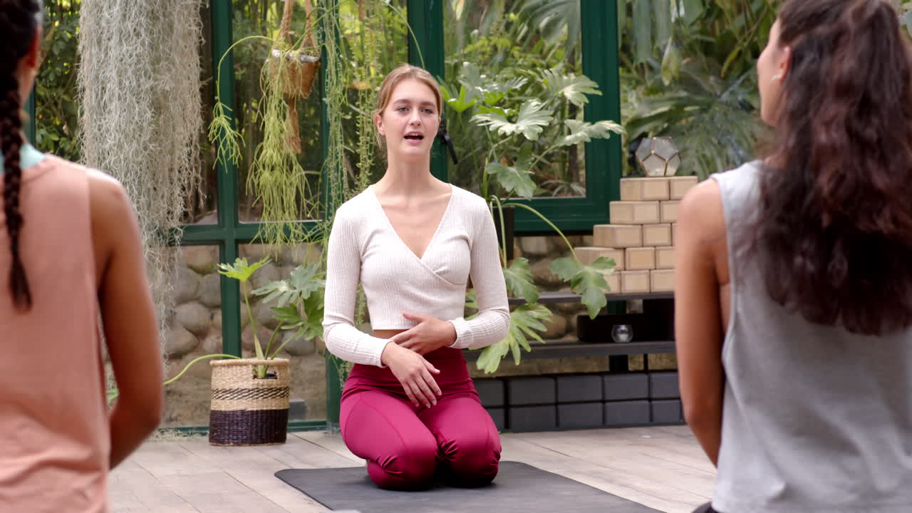 Leading yoga class, woman instructing students on yoga mat in glass house