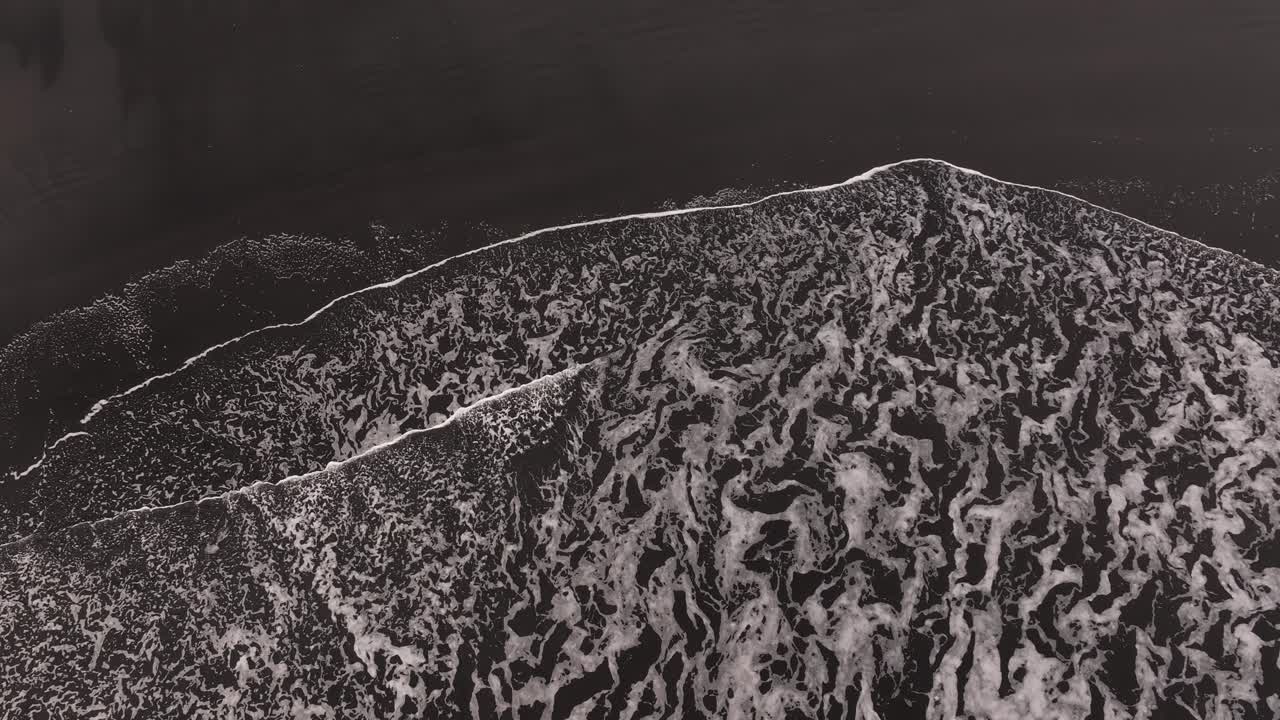 abstract patterns form as ocean surf hits black volcanic shore in Iceland