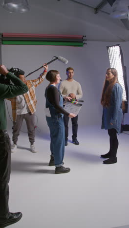 vertical video of frustrated female assistant using clapperboard as actors shoot movie or video in studio with film crew and director shot in real time