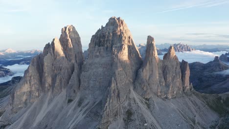 aerial approaching shot of famous tre cime di lavaredo summits in italy during sunrise - beautiful cloud ceiling in background - high angle flight