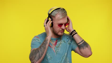hombre alegre y atractivo escuchando música a través de auriculares y bailando discoteca burlándose de divertirse
