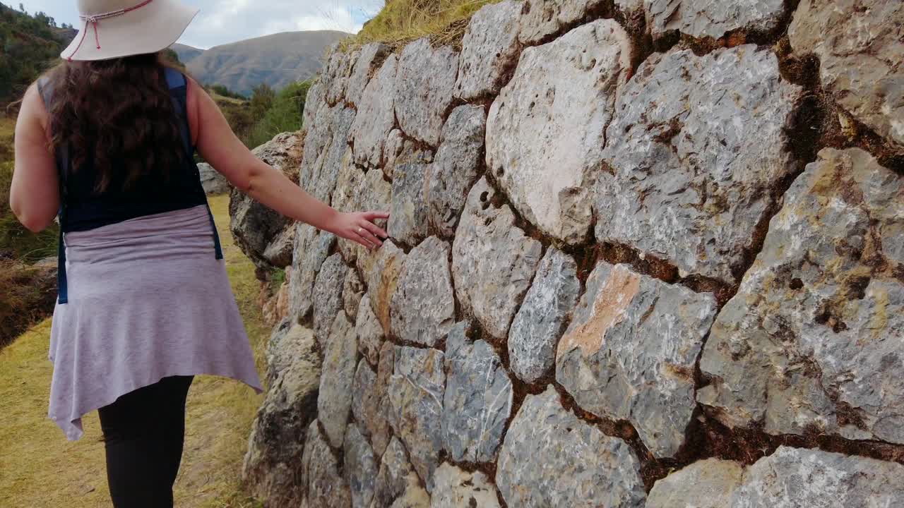 Caucasian woman tourist gently walks alongside old terraced inca ruins of Inkilltambo, Cusco, Peru. Close up reveal shot