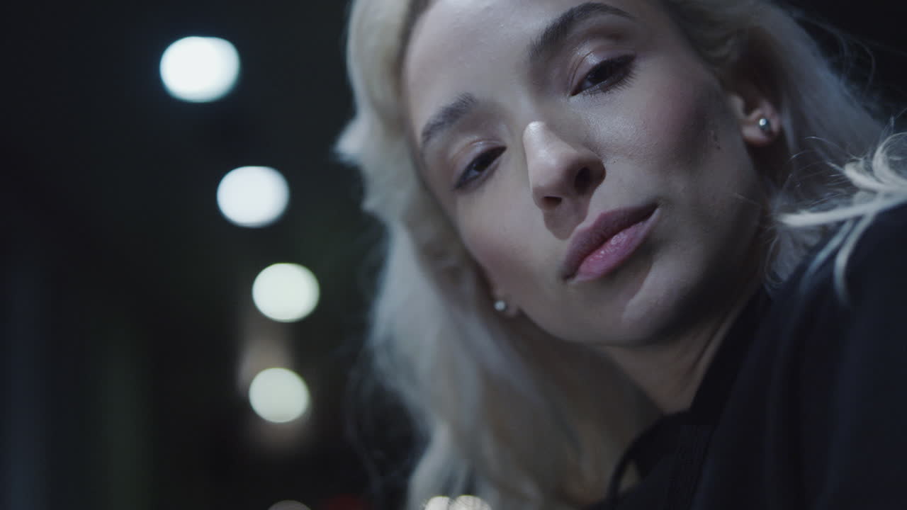 금발 여자 모델 얼굴은 밤의 도시 불빛에서 카메라를 감각적으로 보고 있습니다.