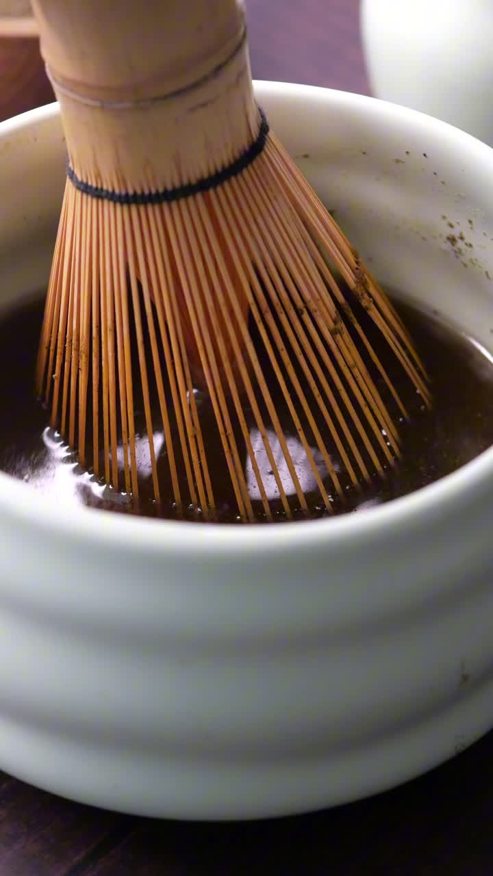 Primo piano di frusta di bambù che mescola tè matcha in una ciotola bianca