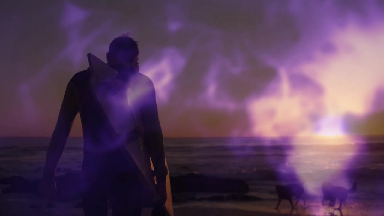 Surfer emerging from water and stepping onto sand amid purple flares appreciating sunset horizon
