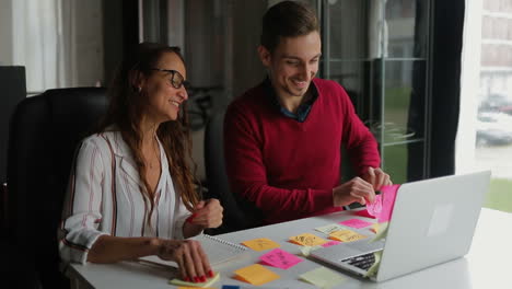 Smiling-man-and-woman-waving-to-camera-and-showing-notes.