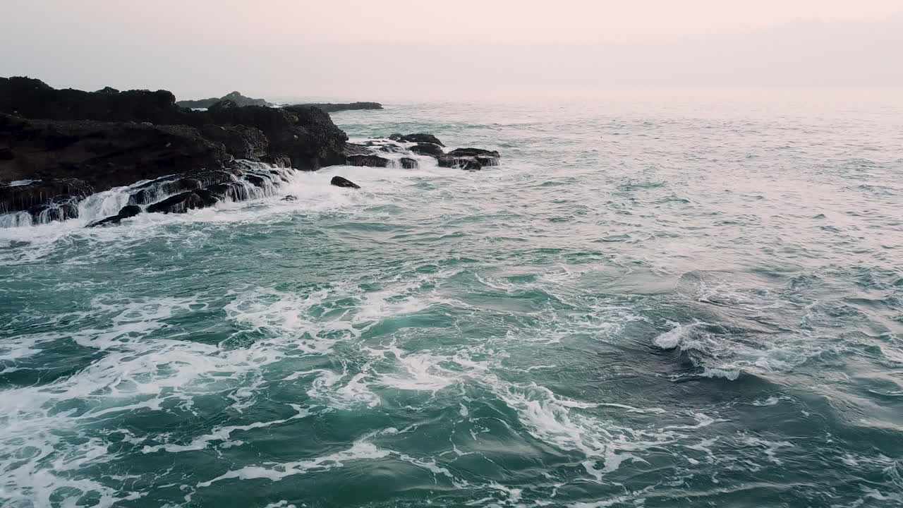 Un'onda si infrange contro una grande formazione rocciosa a Laguna Beach, California, in una giornata nuvolosa