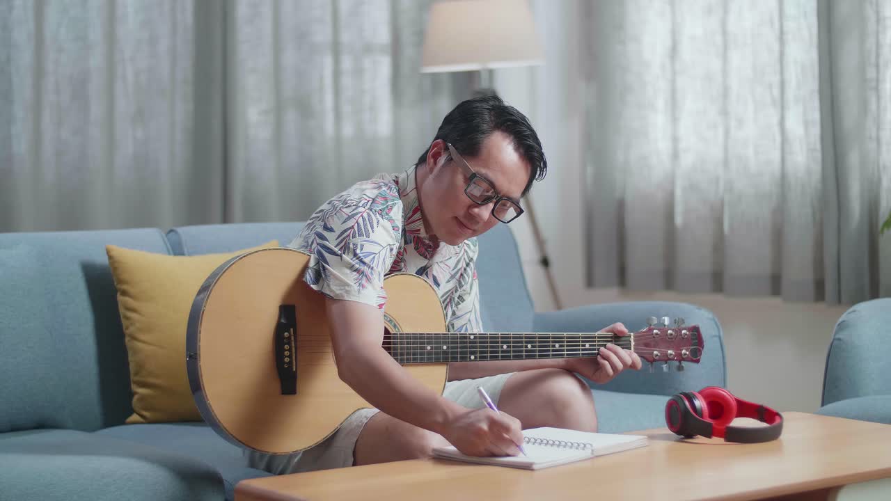 Compositore asiatico che suona la chitarra e compone musica su un taccuino a casa