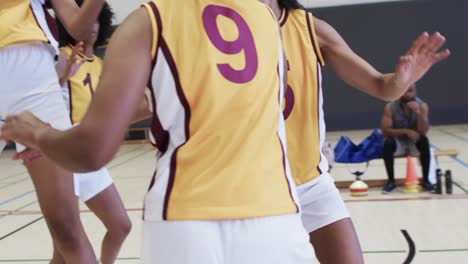 Diverse-female-basketball-team-training-with-male-coach-in-indoor-court,-in-slow-motion