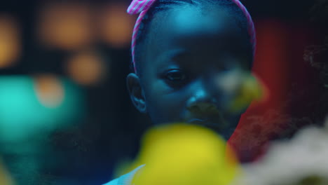 african american girl looking at fish in aquarium curious child watching colorful sea life swimming in tank learning about marine animals in underwater ecosystem inquisitive kid at oceanarium