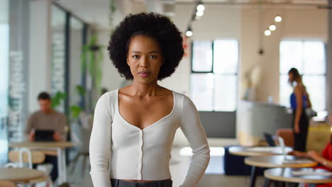 Portrait-Of-Smiling-Businesswoman-Standing-In-Busy-Modern-Open-Plan-Office