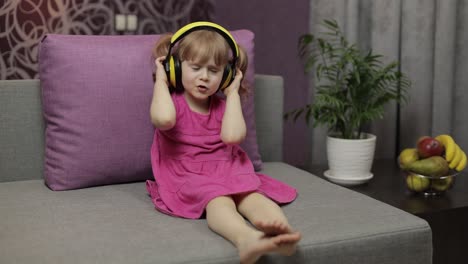 Little-child-girl-in-headphones-enjoying-listen-music.-Dancing-on-sofa-at-home