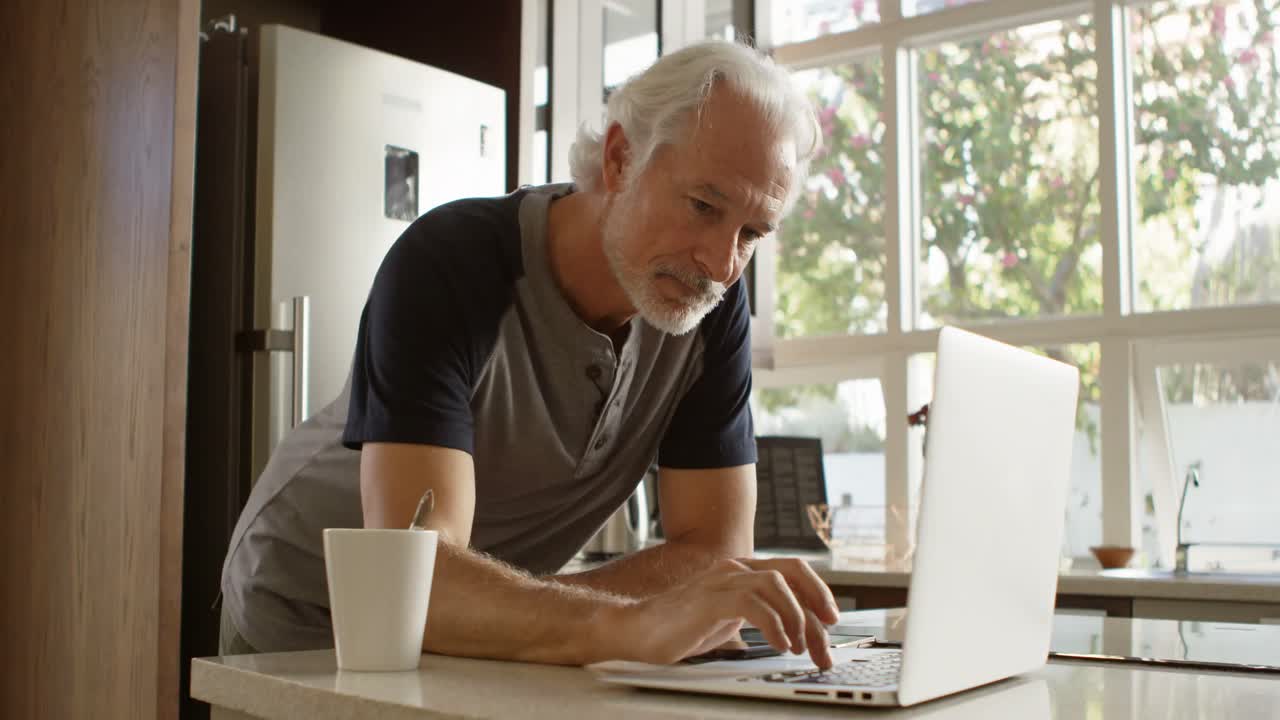 Senior man using laptop in kitchen 4k