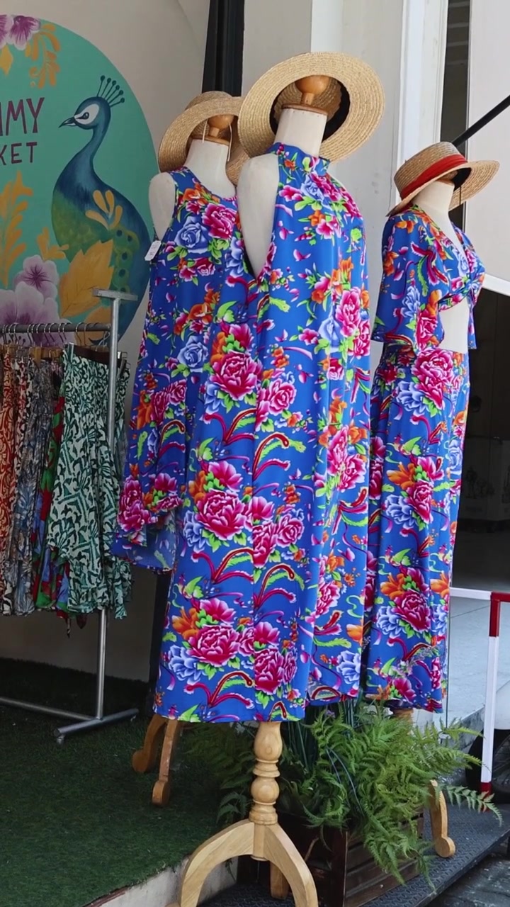 Abiti floreali blu colorati e cappelli di paglia esposti su manichini di legno in una boutique.