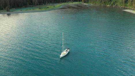 White-Sailboat-Floating-On-Calm-Lake-With-Forest-On-Mountain-In-Alaska