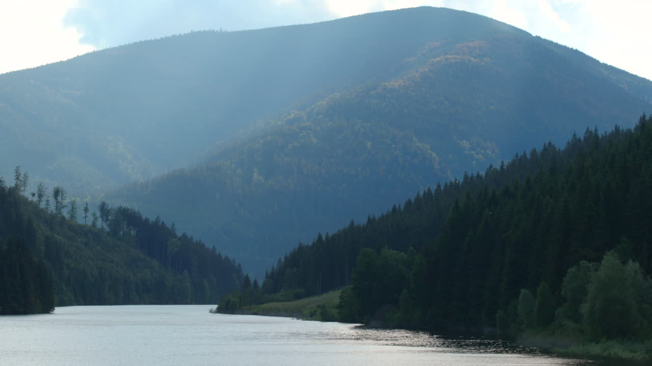 Zoom in Sance drinking water reservoir with a natural valley full of hills and mountains around the water level which moves in a strong wind