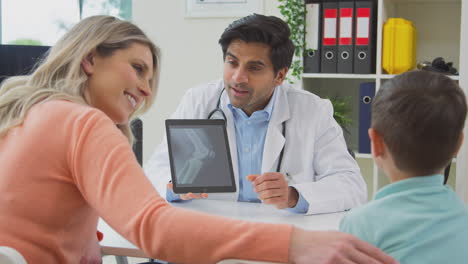 doctor or gp in white coat meeting mother and son for appointment looking at scan on digital tablet