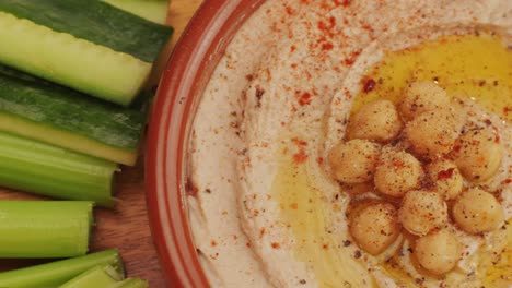 hummus among fresh vegetables on table top view. hummus garnished with chickpeas, olive oil, spices and greens. hummus or fava, a hearty snack of legumes. kosher healthy vegan food. lean, vegetarian dish